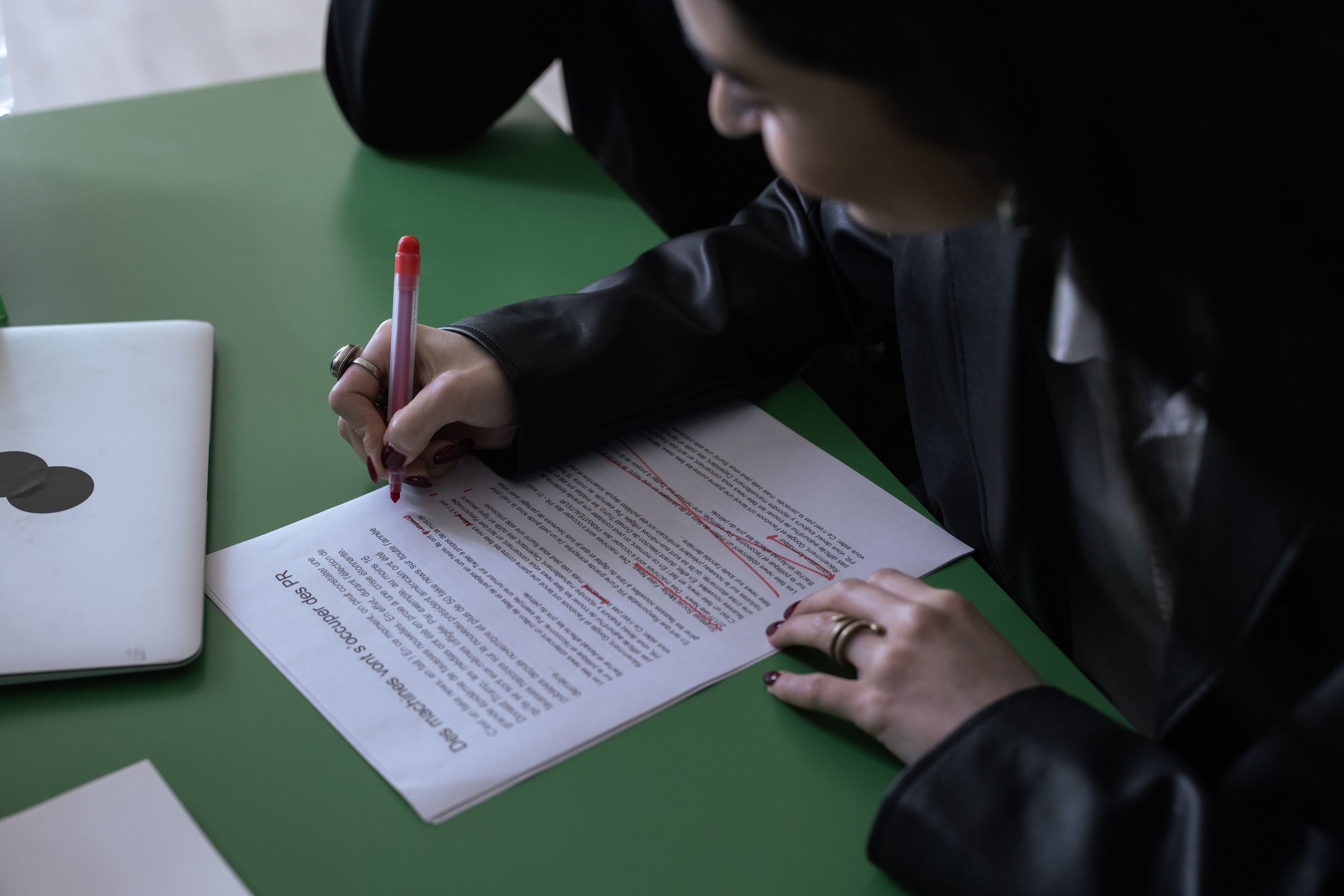 Una abogada corrige con lápiz rojo un documento impreso sobre una mesa.