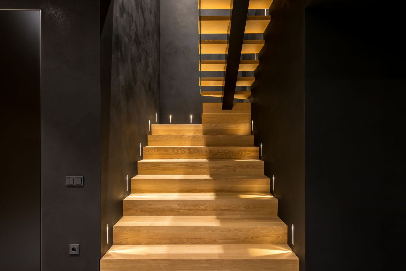 Interior of contemporary multistory apartment with creative wooden stairs and straight dark walls